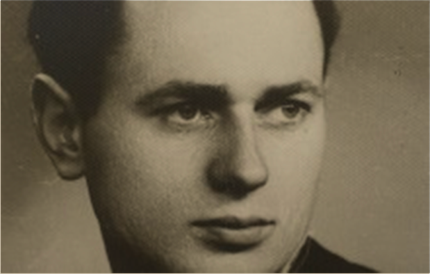 Czarno-białe zdjęcie portretowe Janusza Tomaszewskiego. Mężczyzna ma wydatne czoło, ciemne włosy i nisko osadzone brwi. Ubrany w czarny garnitur, białą koszulę i ciemny krawat.
